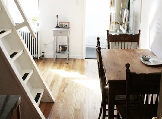 Blick durch das Brooklyn Heights Mikroapartment mit Esstisch, Stühlen, Beistelltisch und Treppe (links) offenem Treppenregala