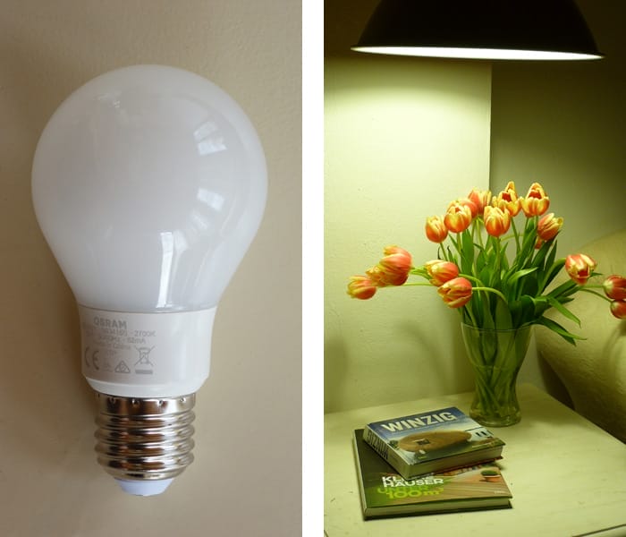 Eine OSRAM LED-Lampe neben einem Nachttisch mit indirekter Beleuchtung, einer Vase mit Tulpen und zwei Büchern