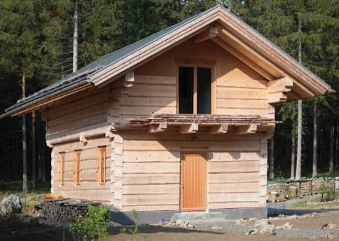 Neues Holzhaus in Blockbauweise, umgeben von einem Nadelwald
