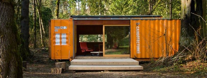 Oranger Seecontainer des Unternehmens Cargotecture, umgebaut als kleines Wohnhaus im Wald, mit Terrasse und rotem Stuhl
