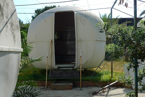 Zwei verwahrloste, weiße, runde BANGA-Minibungalows im Freien, Gras mit mediterranen Pflanzen