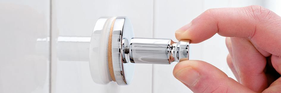 Finger schiebt Haken in zylinderförmige Halterung an einer weißen Wand