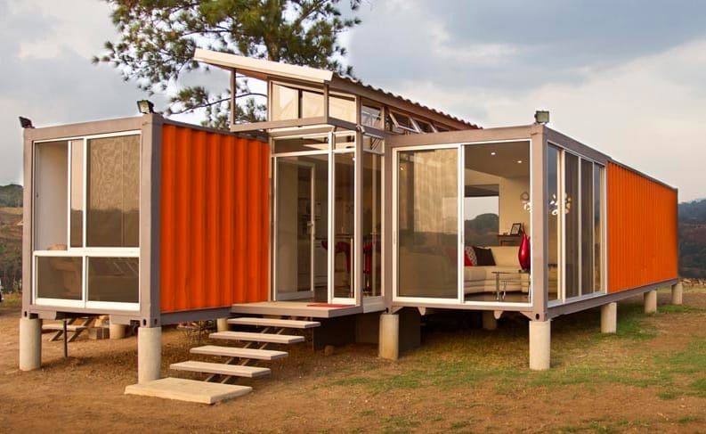 Rostbraunes Tiny House aus Seecontainern mit Treppe und großen Fenstern auf einer Wiese