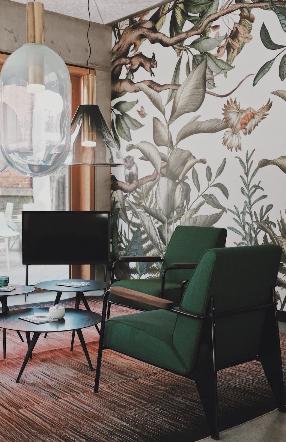 Wohnzimmer mit Dschungel-Tapete, zwei dunkelgrünen Sesseln, modernen Hängelampen in Glas und schwarzen Couchtischen