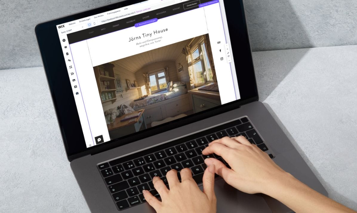 Hände tippen auf einem Laptop, der die Wix.com-Oberfläche mit "Jörns Tiny House" und dem Bild eines Tiny House ansprechenden