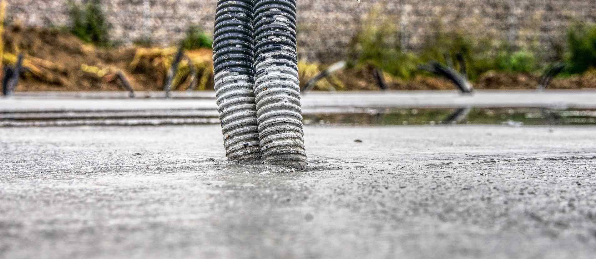 Zwei gerillte graue Rohre ragen aus einer grauen Betonfläche, im Hintergrund Erdreich und Schotter