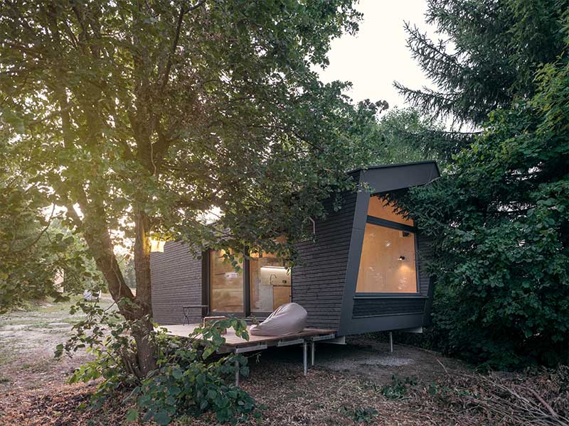 Ein modernes, dunkles Minihaus aus Holz mit großen Fenstern und einer kleinen Terrasse im Grünen