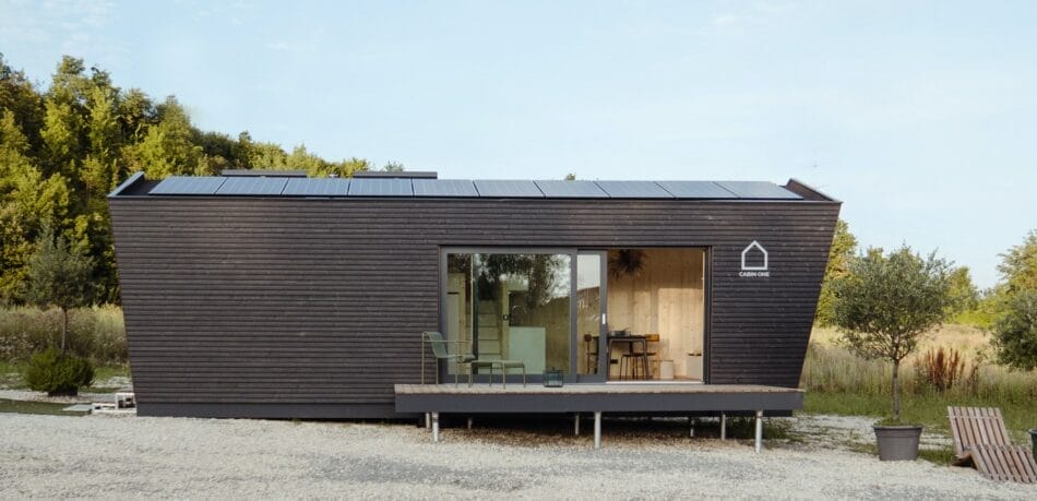 Modernes "Cabin One" Modulhaus mit dunkler Holzfassade, großer Glasfront und Solarpaneelen auf dem Dach