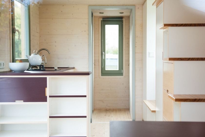 Heller Innenraum eines Tiny House aus Holz mit kleiner Küche und schmalem Fenster am Ende gelegenen Gang, das zu einem Fenste