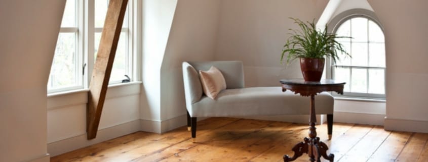 Eine hellgraue Chaiselongue mit Kissen steht in einer Dachschräge, daneben ein Beistelltisch mit Pflanze