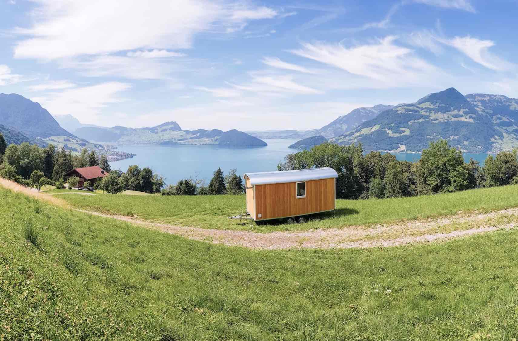 Holz-Tiny-House auf Wiese mit See und Bergpanorama