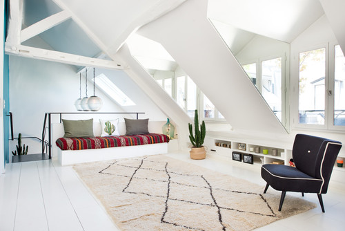Großer, heller Dachzimmer-Wohnraum mit weißem Boden, Dachschrägen, Fensterfront, Sitzbank und beigem Teppich