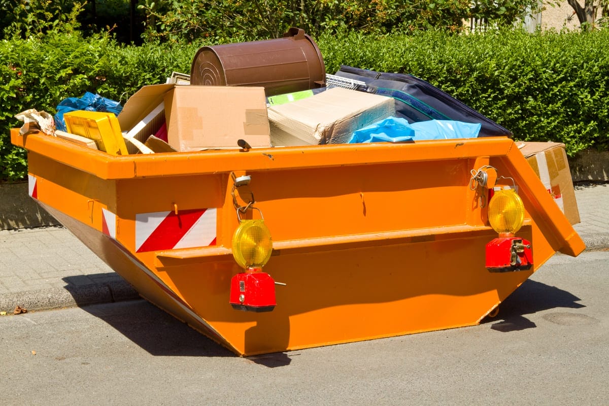 Orangener Container auf einer Straße, gefüllt mit Umzugskartons, Müllsäcken und Hausrat