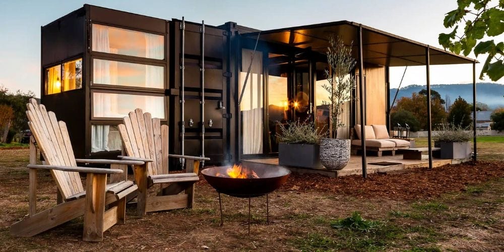 Ein schwarzes, modernes Containerhaus mit großer Außenterrasse, auf der Loungemöbel und Pflanzen stehen