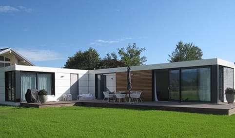 CUBIG Modulhaus in L-Form, mit weißer und holzverkleideter Fassade, auf einer großen Holzterrasse im Garten