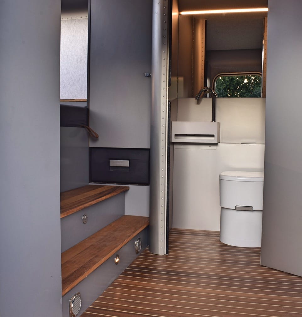 Blick ins Innere des LUME Traveler mit Holzboden, Treppe und sichtbarem WC-Bereich mit Waschbecken und Armatur