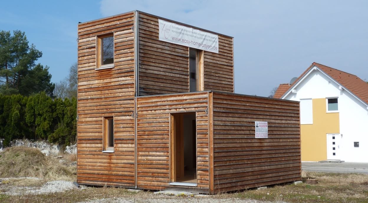 Doppelgeschossiges Minihaus mit Holzverkleidung und der Webadresse easy-home-bayern.de auf einem Schild