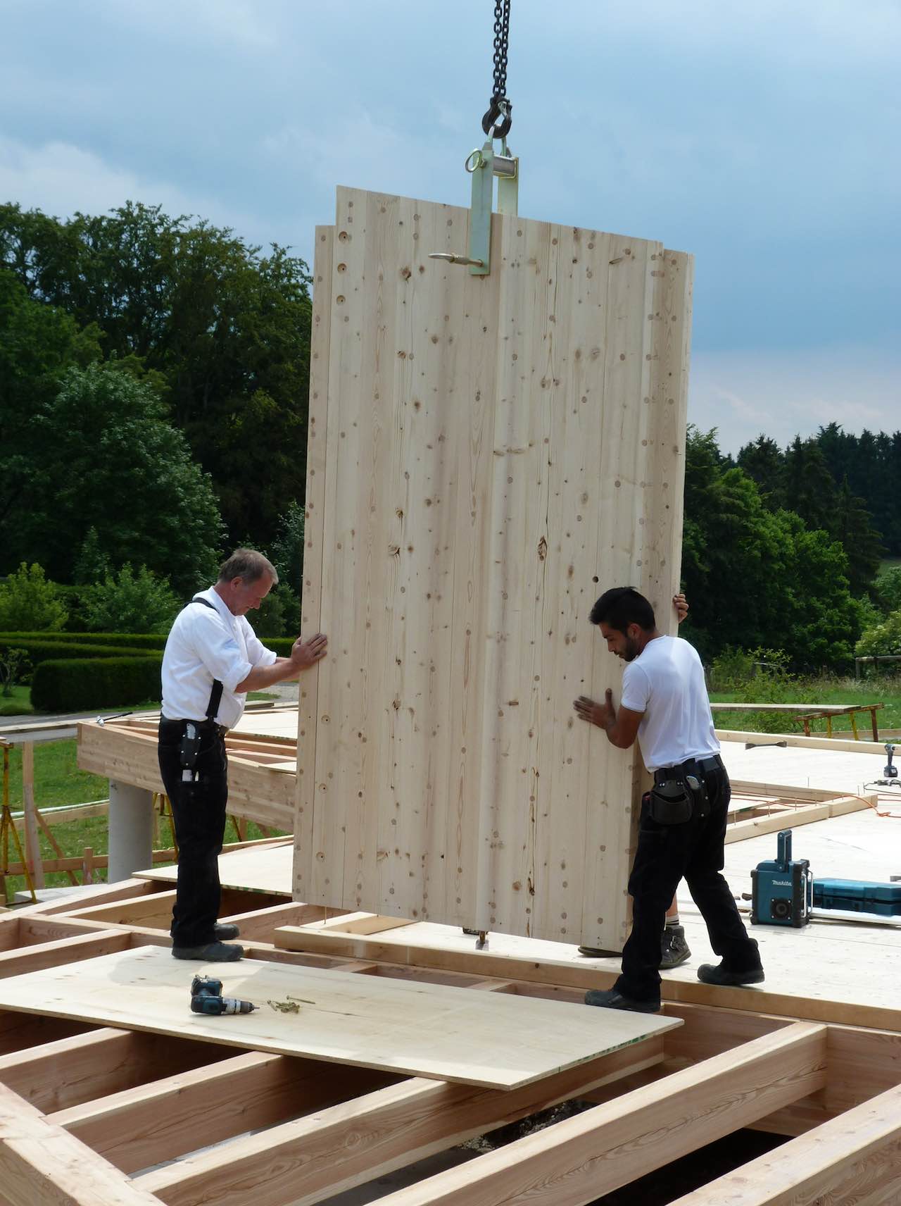 Zwei Männer platzieren Bauholz für den Hausbau auf einer Holzkonstruktion, die von einem Kran gehalten wird