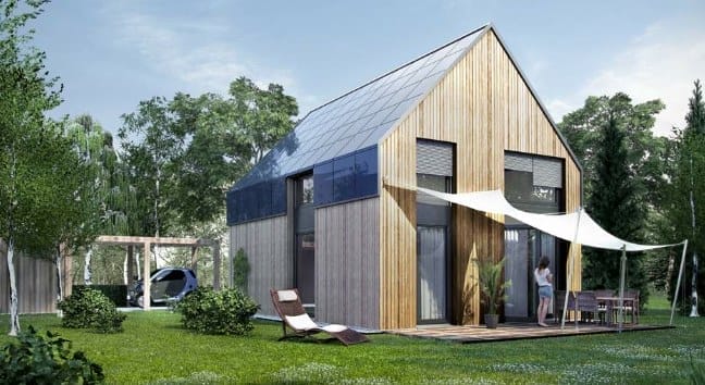 Modernes Holzhaus mit großen Fenstern, Solardach, Terrasse mit Gartenmöbeln und Liegestuhl im Vordergrund