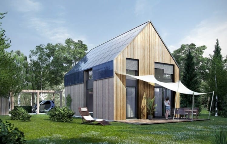 Modernes Holzhaus mit Solardach, davor eine Terrasse mit Sonnensegel und Gartenmöbeln im Grünen
