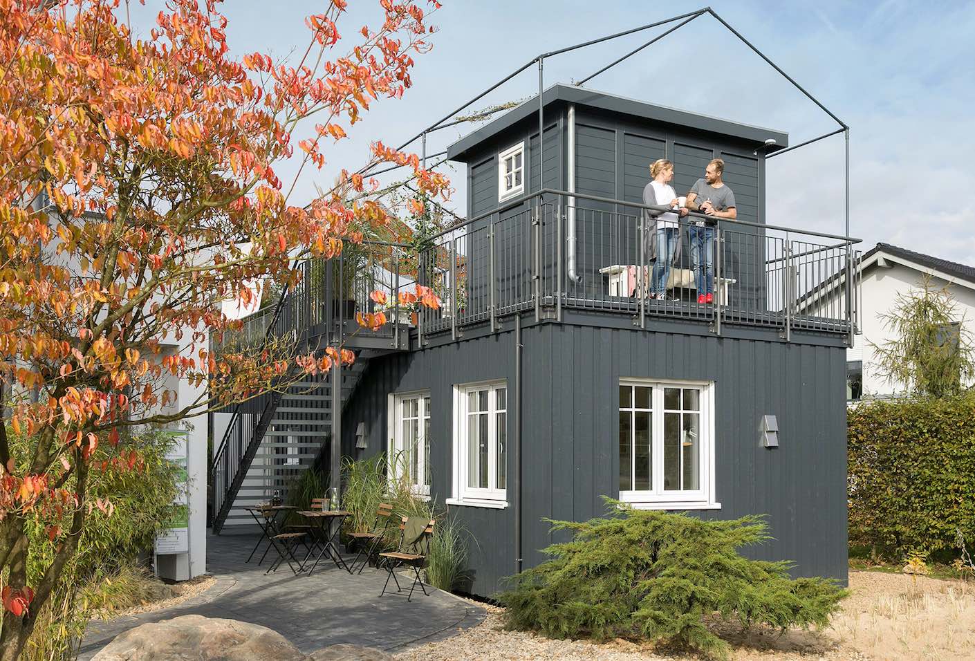 Ein doppelstöckiges Minihaus mit dunkelgrauer Holzfassade und weiß eingerahmten Fenstern