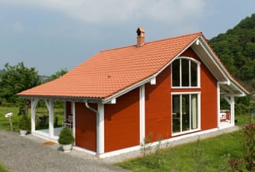 Rotes Minihaus “Oceanside Retreat” von Creative Cottages LLC mit orangerotem Ziegeldach, großen Fenstern und Veranda