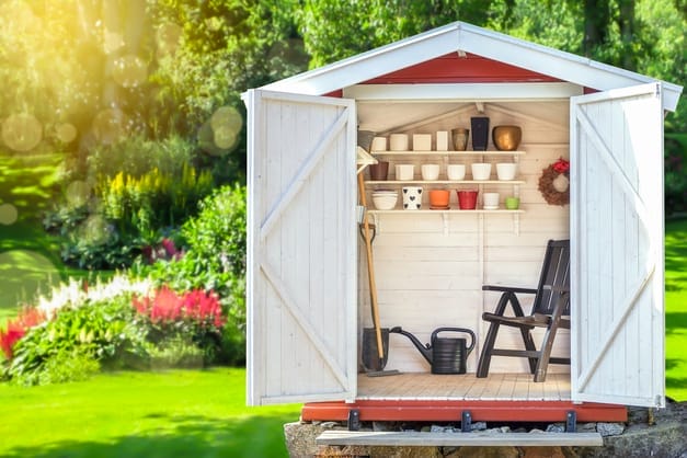Offener Geräteschuppen aus Holz mit Gartenwerkzeugen, Gießkannen und Blumentöpfen auf Regalen