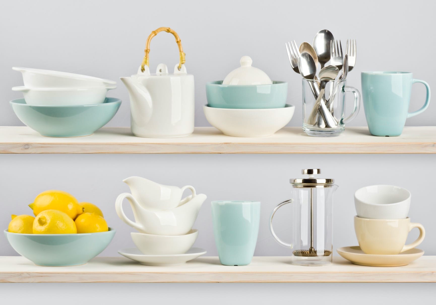 Zwei Holzböden mit Küchenutensilien: Teekanne, Tassen, Schüsseln, Besteck, French Press und Zitronen