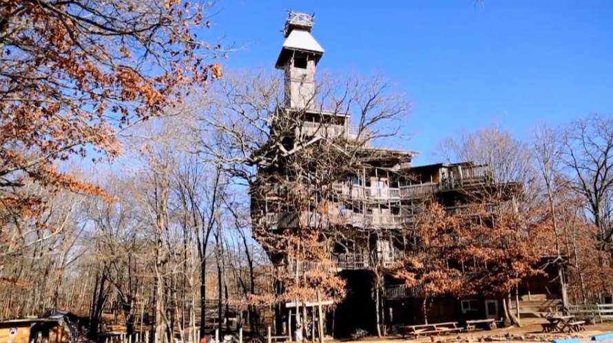 Baumhaus mit vielen Etagen und Turm, umgeben von Bäumen mit herbstlichem Laub und kahlen Ästen