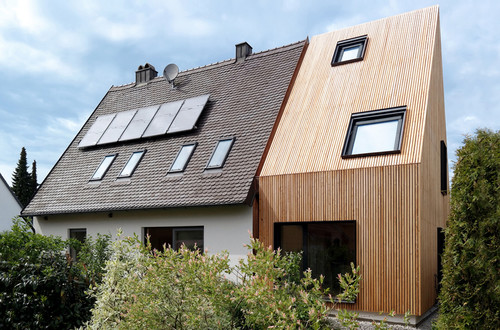 Anbau an ein Siedlerhaus mit vertikaler Holzverkleidung und großen Fenstern sowie Solarpaneelen auf dem Bestandsdach