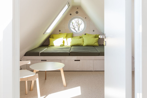 Helles, kleines Schlafzimmer im Dachgeschoss mit Bett und Stauraumschubladen, darüber eine Giebelwand mit Fenstern