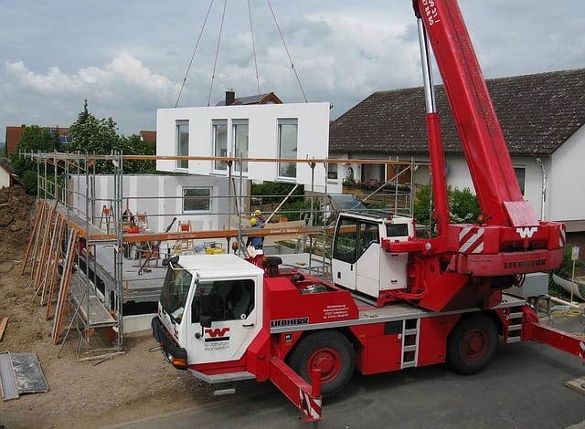 Ein roter Kran der Marke Liebherr setzt ein weißes Modulhaus-Element auf eine Baustelle