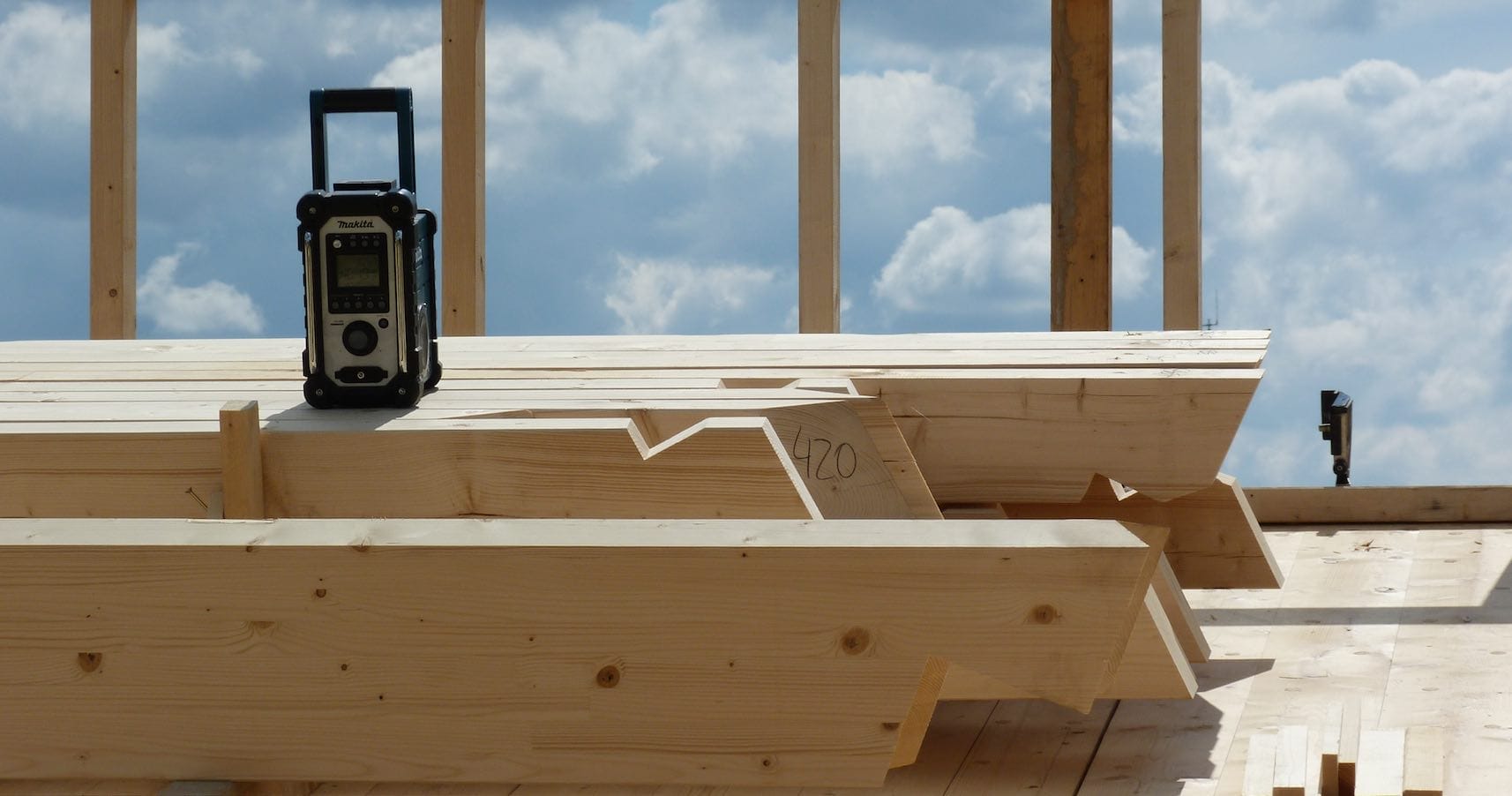 Nahaufnahme eines Baustellenradios der Marke Makita auf einem Stapel Bretter eines Holzständerwerks aus hellem Fichtenholz