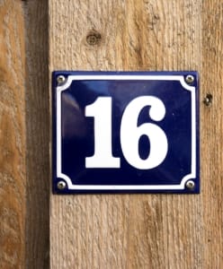 Eine blaue Emaille-Hausnummer „16“ auf einer Holzwand