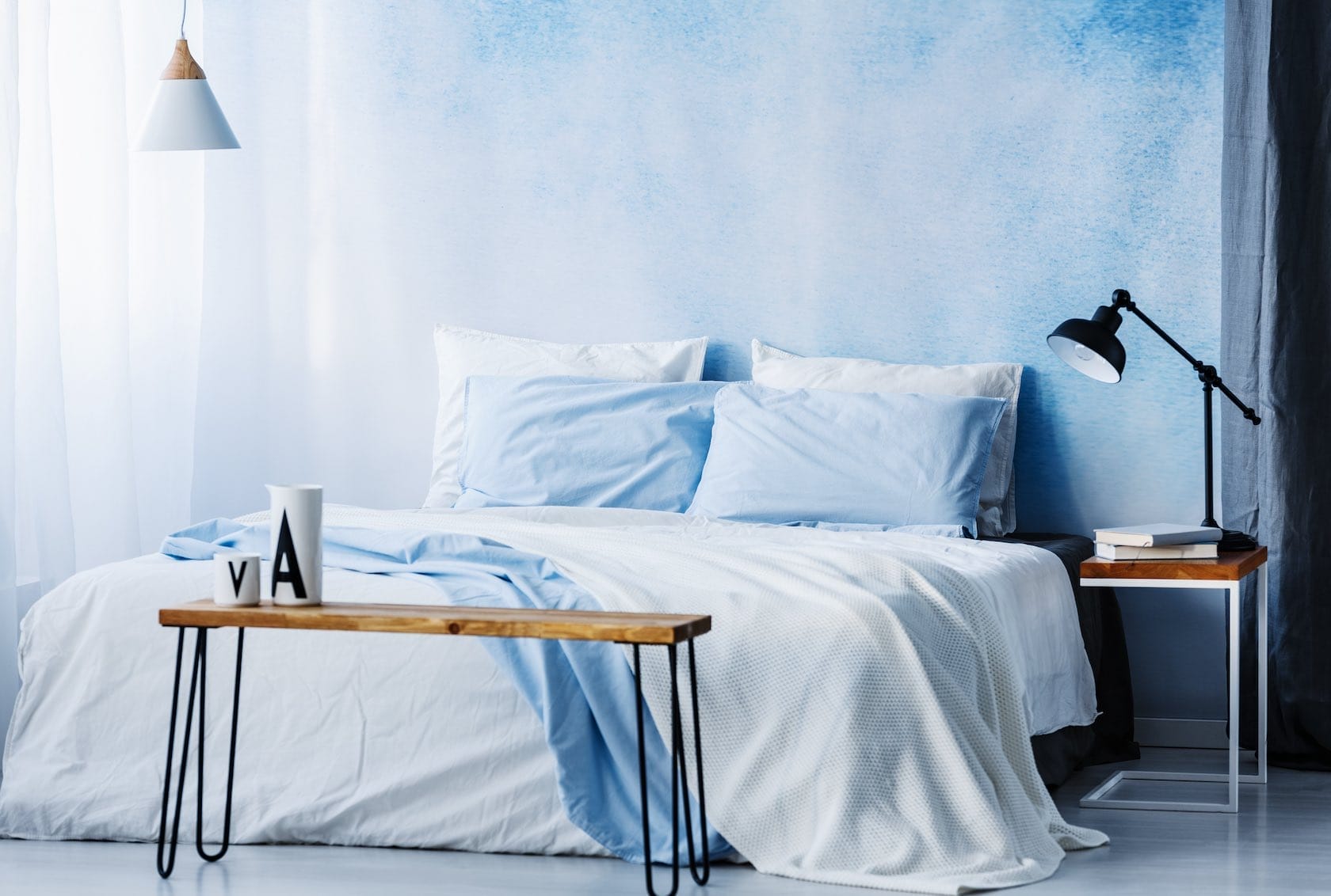 Schlafzimmer mit blau-weißer Wandgestaltung, weißer Bettwäsche und blauen Kissen