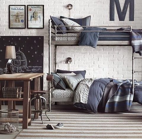 Ein Etagenbett aus Metallgestell in einem Zimmer mit weißen Ziegelwänden und einem Schreibtisch mit Weltraum-Tafel
