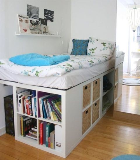 Bett aus weißen IKEA Kallax Regalen gebaut, mit Büchern und Körben als Stauraum, blauer Bettbezug