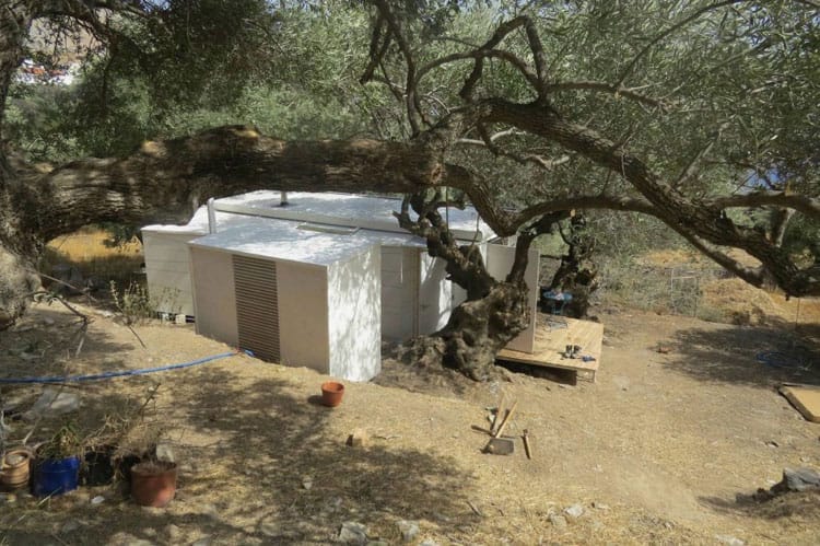 Mobiles Wohnmodul in hellen Tönen, umgeben von Olivenbäumen auf einem kargen Hang auf Kreta