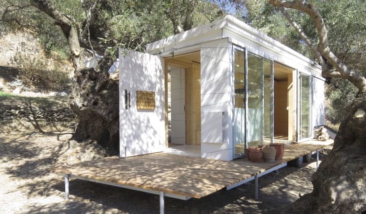 Ein kleines, weißes "House on Wheels" mit großer Holzterrasse steht zwischen Olivenbäumen auf Kreta
