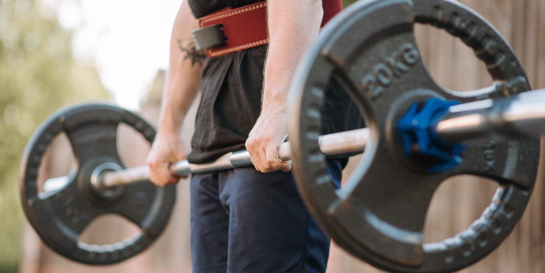 Eine Person in Sportkleidung stemmt eine Langhantel mit 20 kg Gewichtscheiben
