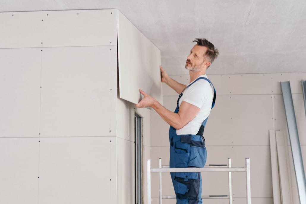 Handwerker in blauer Latzhose montiert weisse Gipskartonplatten an Decke und Wand