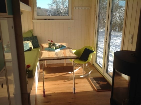 Innenansicht eines Tiny Houses mit Holzboden und weißen Holzpaneelen, Blick nach draußen in verschneite Landschaft