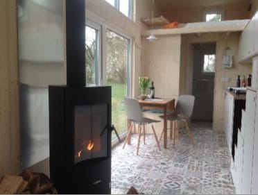 Wohnraum eines Tiny House von Tiny House Design mit Schwarzem Holzofen, Esstisch und Küche