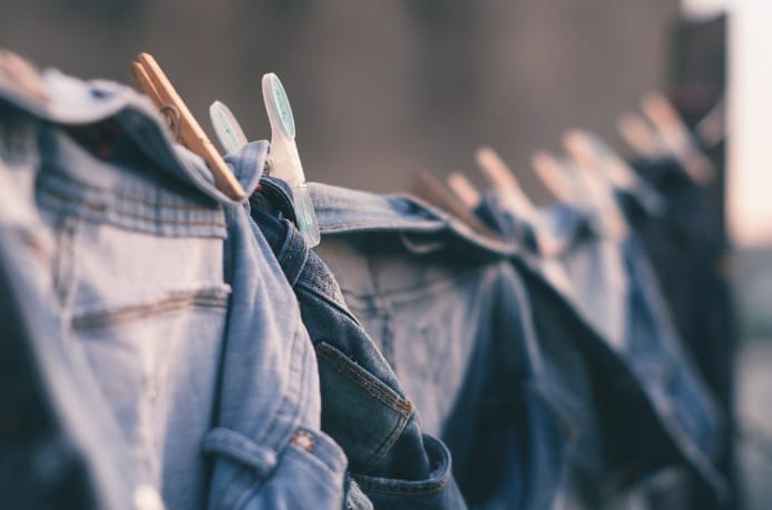 Jeans und andere Kleidungsstücke hängen mit Wäscheklammern auf einer Wäscheleine im Freien