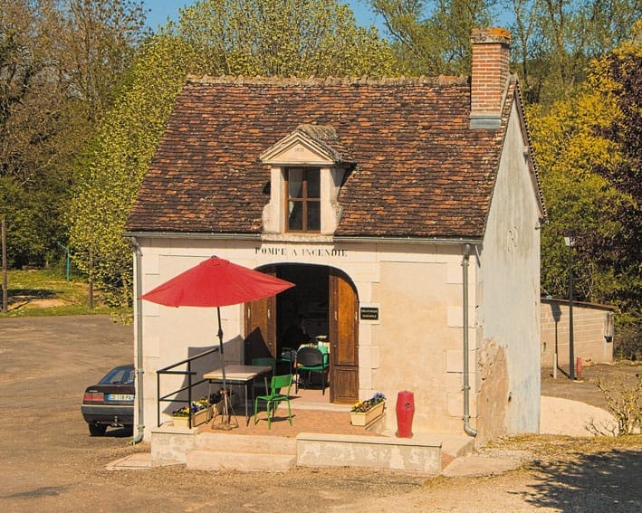 Kleines Gebäude mit Ziegeldach, Kamin, rotem Sonnenschirm und Bistro-Tisch auf einer kleinen Terrasse