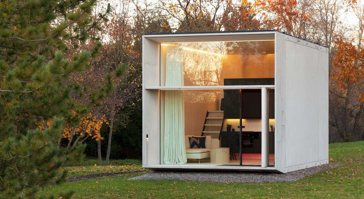 Modernes zweigeschossiges Minihaus aus hellem Holz mit großen Glasfronten in einem Herbstwald