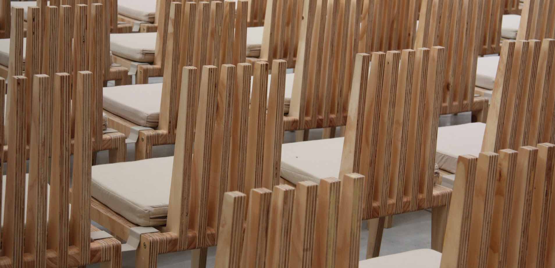 Reihen von hellen Holzstühlen mit hellen Sitzkissen, die Rückenlehnen bestehen aus einzelnen Holzlatten
