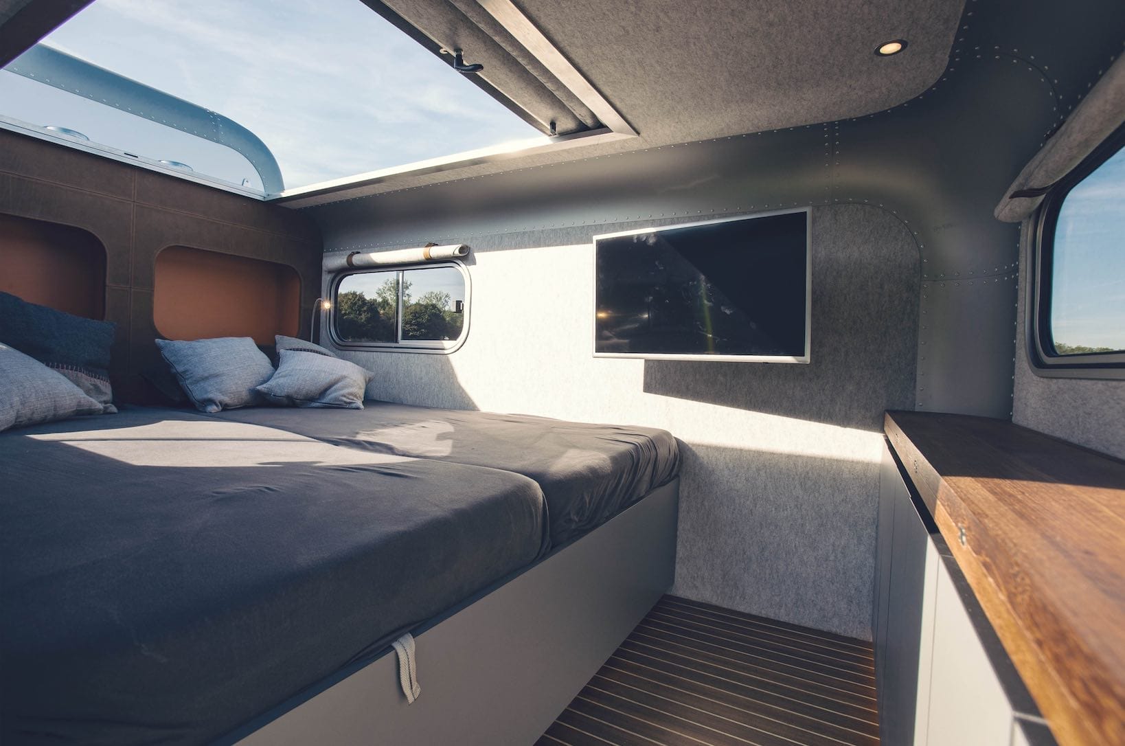 Innenraum des LUME Traveler mit Doppelbett, Panorama-Faltdach und einem Fernseher an der Wand