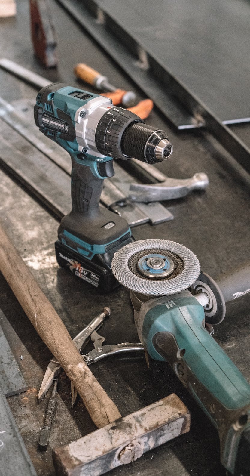 Eine Bohrmaschine und eine Schleifmaschine von Makita liegen neben einem Hammer und Schraubenziehern auf einer Werkbank