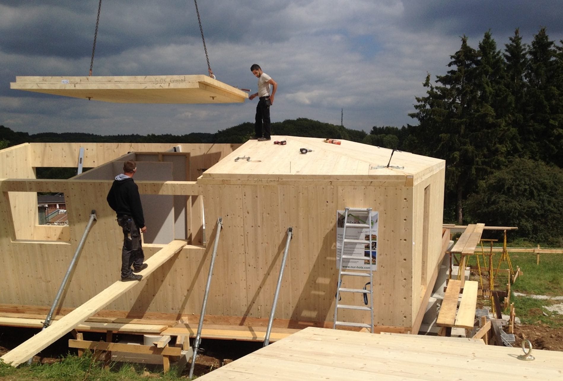 Zwei Bauarbeiter beim Aufbau eines energieeffizienten Minihauses aus Holzfertigteilen mit einem Kran